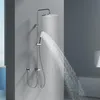 A modern chrome shower system with a rainfall showerhead and a handheld showerhead is shown in operation against a gray wall. Podgląd zdjęcia produktu