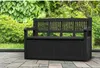 A black storage bench is placed on a paved patio in front of lush green foliage. Produktbild-Vorschau