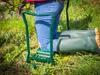 A person is kneeling in the grass using a gardening stool. Produktbild-Vorschau