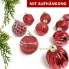 A collection of red Christmas ornaments arranged on a white background, with green foliage on the left. Produktbild-Vorschau