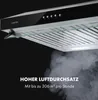 A close-up, angled shot of a black and silver range hood with a glass shelf, set against a dark background. Smoke is emanating from below the hood. Produktbild-Vorschau