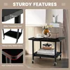 A collage of images showing a black two-tier rolling side table, highlighting its sturdy features such as thickened panels, heavy-duty metal frame, and rounded corners. The main image shows the table with decorative items on it. Produktbild-Vorschau