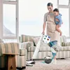 A woman is vacuuming while holding a baby in a living room. Produktbild-Vorschau