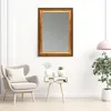 A mirror with an ornate frame hangs on a white wall above a small side table with decorative items. A chair and a plant are also visible in the scene. Produktbild-Vorschau