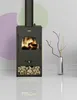 A black wood-burning stove with a fire burning inside, placed on a white floor with a reflection. The background features a wall with abstract pastel circles and a vase with decorative branches. Anteprima dell’immagine prodotto