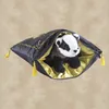 A plush badger toy peeking out of a dark grey drawstring bag with gold lining and yellow tassels. Produktbild-Vorschau