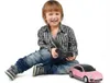 A young boy is sitting on the floor, holding a remote control, with a pink toy car next to him. Náhled obrázku produktu