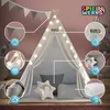 A child's play tent set up indoors, decorated with star-shaped lights and a garland, with various accessories like pillows and a floor mat. Podgląd zdjęcia produktu