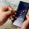 A person's hands are holding a smartphone and a stylus, interacting with the screen which displays a menu of options. Podgląd zdjęcia produktu