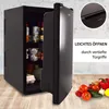 A black mini-fridge with its door ajar, revealing food and drinks inside. The fridge is placed on a wooden floor against a textured gray wall. A small inset image shows a detail of the fridge handle. Vegetables are arranged in the foreground. Anteprima dell’immagine prodotto