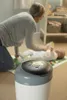 A mother is changing her baby's diaper on a changing mat, with a diaper pail in the foreground. Voir les images du produit