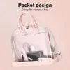 A pink and clear handbag with a laptop, phone, and other accessories inside, set against a pink background. Produktbild-Vorschau