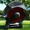 A close-up view of a rotary mower with a red cutting disc and black housing, set against a grassy background with trees and a blue sky. Produktbild-Vorschau