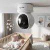 A baby monitor camera is mounted on the ceiling, overlooking a crib with a baby inside. Náhled obrázku produktu