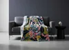 A colorful tropical-patterned blanket draped over a gray sofa in a minimalist room. Podgląd zdjęcia produktu