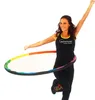 A woman is shown hula hooping with a colorful fitness hoop. Produktbild-Vorschau