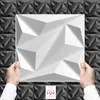 Hands holding a white 3D wall panel in front of a black and gray textured wall. Produktbild-Vorschau