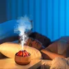 A volcano-shaped aroma diffuser emitting steam sits on a nightstand next to a sleeping couple. Produktbild-Vorschau