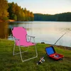 A pink camping chair is set up on a grassy bank next to a lake, with a fishing rod and tackle box nearby. Produktbild-Vorschau