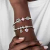 A person's arm wearing two silver charm bracelets with various charms. Podgląd zdjęcia produktu