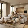 A family is relaxing in a modern living room, with the parents reading a book to their children on a large sectional sofa. The scene includes a coffee table with books and toys, and a glimpse of a kitchen area in the background. Produktbild-Vorschau