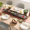 A dining table set up for a meal with an electric grill plate in the center, surrounded by food and place settings. Voir les images du produit