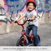 A young boy is riding a red balance bike in front of a graffiti-covered wall. Produktbild-Vorschau