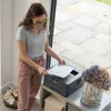 A woman is holding a printed document next to a Brother printer. Produktbild-Vorschau