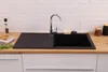 A black kitchen sink with a chrome faucet is installed on a wooden countertop, with a white tiled backsplash behind it. Produktbild-Vorschau