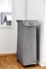 A grey fabric laundry hamper with wheels is shown in a room, next to a white wall and a mirror. Náhled obrázku produktu