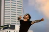A man with tattoos on his arms is celebrating outdoors in front of a tall building. Produktbild-Vorschau