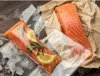 Two raw salmon fillets, one vacuum-sealed with lemon slices and rosemary, on a wooden surface with ice. Náhľad obrázku produktu