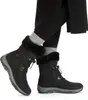 A pair of black winter boots worn by a person, shown from the knees down. Produktbild-Vorschau