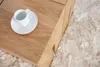 A close-up of a wooden coffee table with a white cup and saucer on it, placed on a fluffy rug. Produktbild-Vorschau