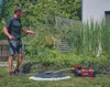 A man is watering plants in a garden with a pump and hose. Produktbild-Vorschau