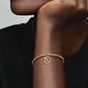 A close-up shot of a person's arm wearing a gold bracelet with a circular charm. Voir les images du produit