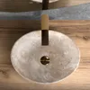A close-up overhead view of a beige stone vessel sink with a gold faucet, set on a wooden surface. Náhľad obrázku produktu