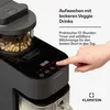 A close-up of a black Klarstein appliance with a hand pressing a button on its touch screen. Cashews are visible inside a transparent container on top of the appliance. Produktbild-Vorschau