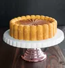 A cake on a white cake stand, on a wooden surface, with a dark background. Produktbild-Vorschau