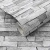 A roll of wallpaper with a stone and concrete pattern is shown, partially unrolled against a background of the same pattern. Produktbild-Vorschau