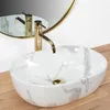 A close-up shot of a marble-patterned vessel sink with a gold faucet, set against a plain background and a wooden surface. Náhled obrázku produktu