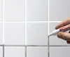 A hand is using a white marker pen to touch up the grout lines between white tiles. Produktbild-Vorschau