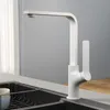 A white kitchen faucet is shown in a modern kitchen setting, next to a sink with a dish rack. Podgląd zdjęcia produktu