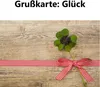 A four-leaf clover with a red and white checkered ribbon tied around its stem, placed on a wooden background. Produktbild-Vorschau