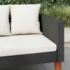 Close-up of a black rattan sofa with white cushions, set outdoors with greenery in the background. Produktbild-Vorschau