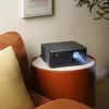 A projector is placed on a side table next to a sofa in a living room. Náhled obrázku produktu