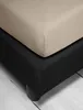 A close-up view of a beige fitted sheet on top of a black bed base. Produktbild-Vorschau