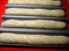 Four unbaked baguettes are arranged in a perforated baking tray. Náhled obrázku produktu