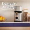 A coffee machine brewing espresso, with coffee beans in jars and fruit in a bowl on a kitchen counter. Voir les images du produit