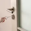 A hand is using a small metal tool to open a door lock. Produktbild-Vorschau